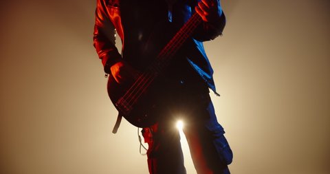 An amazing rock music player performing. Grunge musician is playing rock on bass guitar on stage, making a cool solo in red and blue neon lights 4k footage