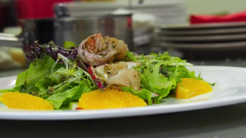 Salad of greens, oranges and shrimp is slowly watered with brown sauce.