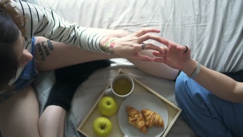 Female hands of young women holding while they sit on bed at home. Couple of lesbian girlfriends Spbd touching affectionate. concept romantic, touch, feminity. girls eating breakfast : vidéo de stock