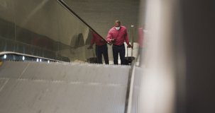 African American man wearing a face masks against air pollution and covid19 coronavirus, using an escalator in a metro station, holding a suitcase and using his smartphone.