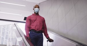 African American man wearing a face masks against air pollution and covid19 coronavirus, using an escalator in a metro station and holding a suitcase.