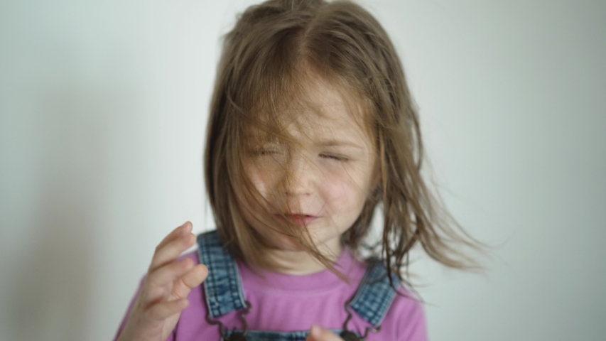 Face of little cute girl when the hair is flying child sweeps away blowing hair from her face indoor on white background.