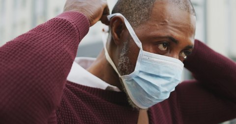 African American man out and about in the city streets during the day, putting on a face mask against air pollution and covid19 coronavirus.