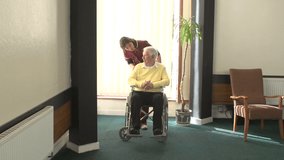 Carer pushes an Elderly Senior man in his Wheelchair in a Nursing Home - Stock Video Clip Footage