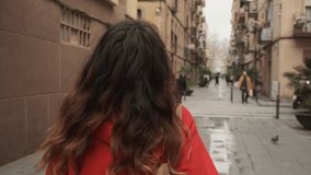 Tracking around shot of beautiful hispanic girl in hoodie dreamily walking through old city street