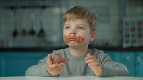 Blonde boy eating Easter chocolate bunnies with dirty face at home on blue kitchen. Happy kid celebrating Easter with colored eggs and chocolate bunnies.  - Powered by Shutterstock - Get 15% off with code: PIKWIZARD15