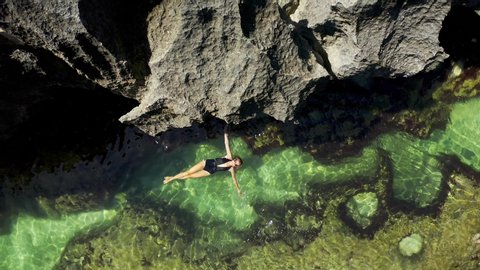 Young beautiful woman swims in a natural pool Angel's Billabong at Broken Beach in Nusa Penida island, Bali in Indonesia. Aerial View 4K