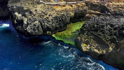 Tourists visits the Angel's Billabong beach at the Nusa Penida island where huge waves are breaking on the rocks. BAILI, INDONESIA - Feb 15, 2020. Aerial View 4K