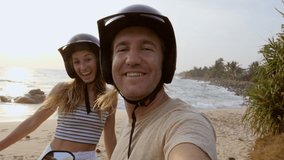 Young couple taking selfie on scooter at sunset by the beach. Two people exploring Sri Lanka with motorbike taking video selfie chatting online with friends sharing adventures 