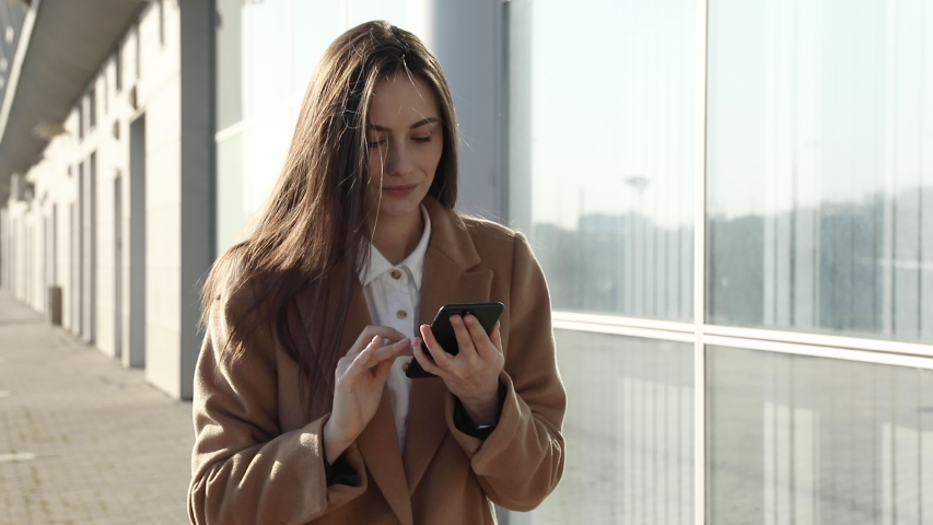 Close up successful businesswoman using phone at street. Serious business woman walking with phone outdoor. Sexy woman messaging on phone at street. Female entrepreneur working with smartphone
