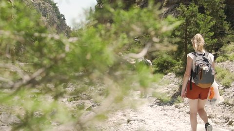 Tourists, hikers and blonde caucasian girl walking on a rocky hiking path along a water creek with bridges running through the narrow Samaria Gorge in Crete, Greece in Slow Motion - Slow Mo 100fps