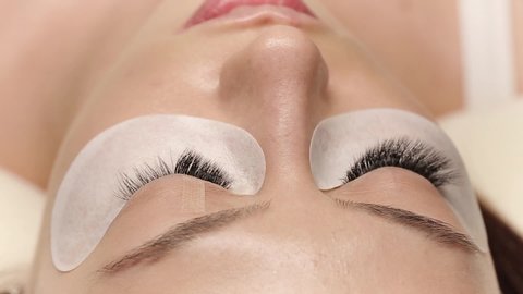 Eyelashes extensions. Fake eyelashes. Eyelash extension procedure.Close up portrait of woman eye with long eyelashes. Professional stylist lengthening female lashes. Master and client in beauty salon.