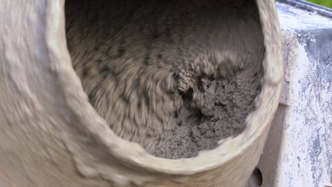 Process of mixing cement slurry with sand and gravel in a concrete mixer at construction site, close up. Technology of manufacture of binding materials used in building and civil engineering