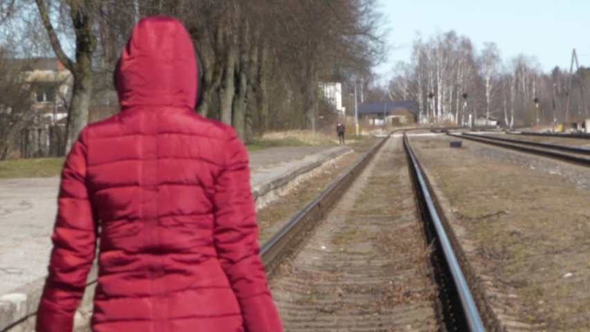 A woman with a suitcase and backpack walks along the railway tracks