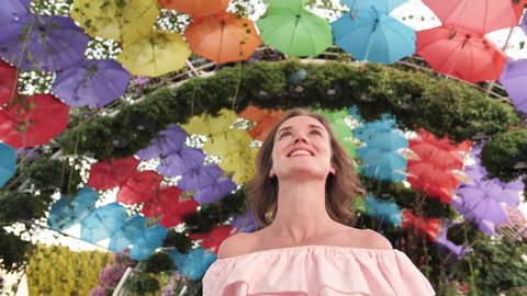 A girl walks on the background of multi-colored umbrellas in a park in the city