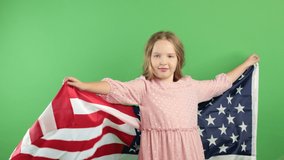 Fun loving blond girl dancing with big american flag outdoors on green background