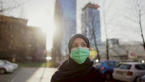 Female Muslim with protective surgical mask.Hijab woman wearing mask in the city.Coronavirus COVID-19 pandemic lifestyle in Islamic country culture.Spiritual praying concerned person.Faith challenge