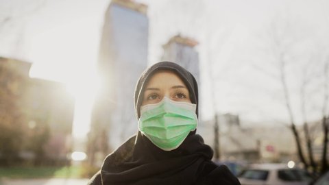 Female Muslim with protective surgical mask.Hijab woman wearing mask in the city.Coronavirus COVID-19 pandemic lifestyle in Islamic country culture.Spiritual praying concerned person.Faith challenge