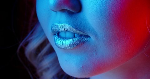 Sensual girl with bright glowing lipstick seductively licking her lips in neon light - nightlife, nightclub concept extreme close up shot 4k footage
