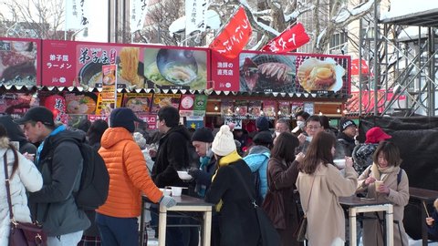 SAPPORO, HOKKAIDO, JAPAN - 11 FEB 2020 : View of street food and drink stalls at Sapporo Snow Festival. One of Japan's most popular winter events. Various kinds of traditional Japanese food are sold.
