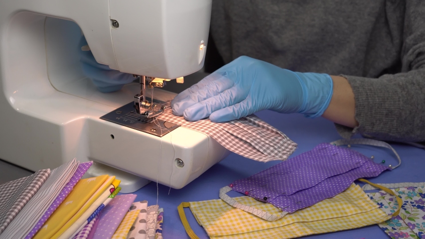Woman volunteer in hand gloves sew reusable cloth protective upcycled face mask with sewing machine at home, making cotton fabric medical mask. Coronavirus Covid-19 virus protection | Shutterstock HD Video #1049930521
