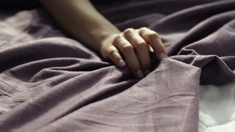 Young woman stay at home during quarantine. Girl's hand holding a satin sheet. Sensual moment of pleasure on bed. Daylight.