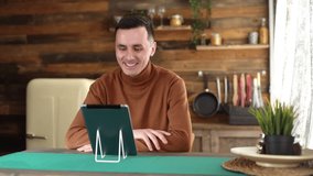 Young cheerful man using tablet computer having online video chat with friends and says goodbye to his while sitting at the table in cozy room. Shooting in slow motion.