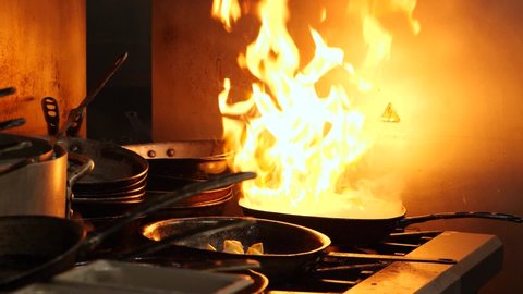 Big flame on the pan. A lot of kitchenware. Dangerous fire in the kitchen. There are metal bowls and pans a well.