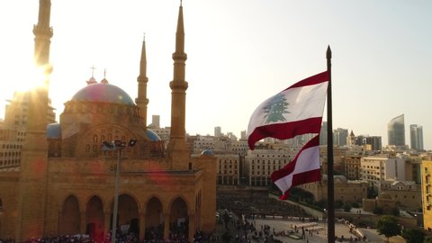 Beirut, Lebanon 2019: sunset turn around track in drone shot passing by the Lebanese flag with mosque, church and sun flaring in the background during the Lebanese revolution