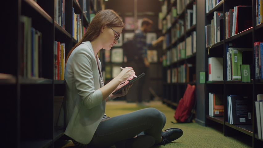 University Library: Beautiful Caucasian Girl Sitting On the Floor, Uses Digital Tablet Computer and Writes Notes for the Paper, Study for Class Assignment. Diverse Group of Students Learning Royalty-Free Stock Footage #1049967715