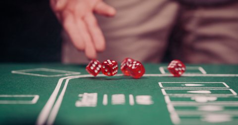 Gambler rolling the dice towards the cam on green poker table shot in 4k super slow motion