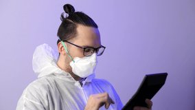 Man in a protective surgical suit and protective medical mask counts on a calculator. Budget for medicine, salary of doctors. Coronavirus or COVID-19 prevention. - Powered by Shutterstock - Get 15% off with code: PIKWIZARD15