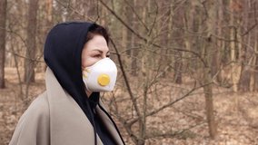 Video footage, a young adult woman in a white protective mask walks through the park on a spring day