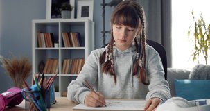 Pretty female teenager with trendy hairstyle in casual clothing sitting at table and drawing colorful paintings. Concept of self development and art