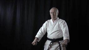 Formal exercises karate are trained by an old male athlete on a black background