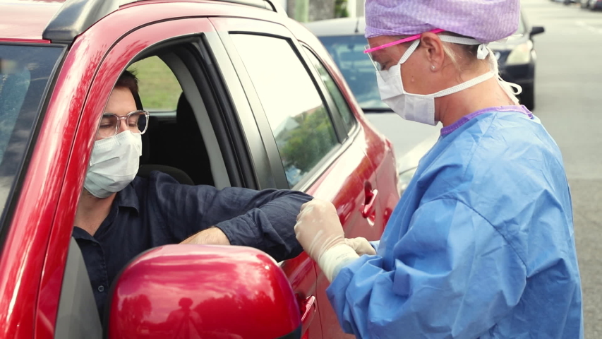 A doctor in a protective suit taking a nasal swab from a driver to test for possible coronavirus infection Royalty-Free Stock Footage #1049998960