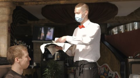 A European-looking waiter in a medical mask serves Latte coffee