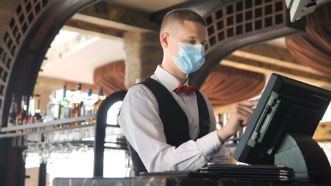 Man or waiter in medical mask at counter with cashbox working at bar or restaurant