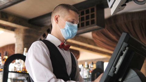 Man or waiter in medical mask at counter with cashbox working at bar or restaurant