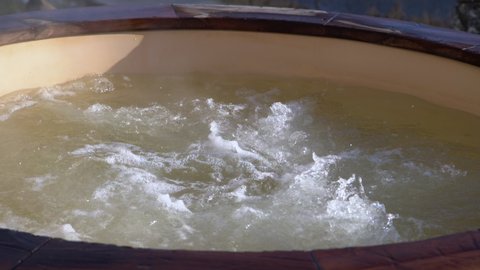 How water swirling in wooden hot tub outside in nature. Enjoying hot steaming pool on a sunny day, private spa treatment. Nobody
