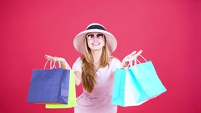 Shopping summer concept. Caucasian woman looks happy while holding shopping bags and standing in the studio. Shot in 4k resolution with red background