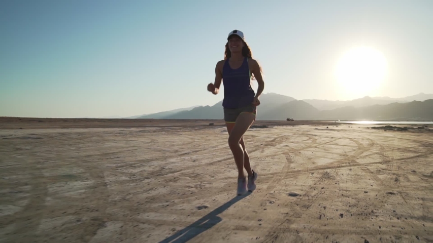 Young fit caucasian girl jogging in dry desert at sunrise rapid slow motion