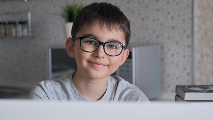 Portrait. Schoolboy doing homework using laptop while sitting at home in the kitchen at the table and looking at the camera with a smile Royalty-Free Stock Footage #1050007456