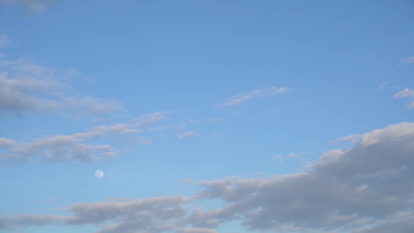 Beautiful big moon in daylight period. Time lapse of many clouds and shiny moon moving fastly along clear blue sky at sunset time. Video shoot in evening 6 of April 2020 during Supermoon (Pink Moon).