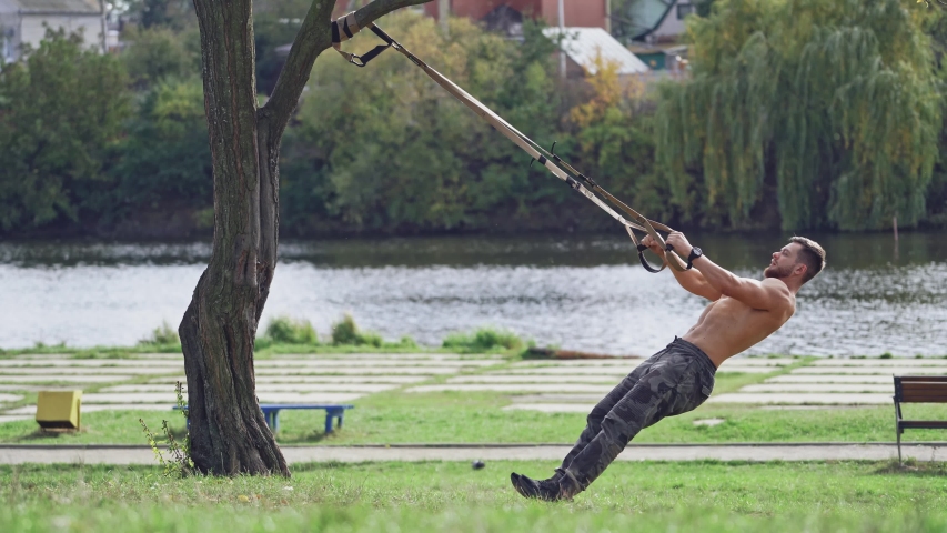 Training in open air. Young man working out by the lake in city park