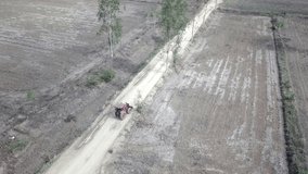 aerial static view of a small tractor driving over a dirt road through the dry field