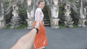 Follow me to Asia, young smiling woman leading boyfriend to beautiful old stairs with dragons at balinese temple, wearing traditional orange sarong, Lempuyang Temple, Bali, Indonesia