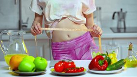 Cropped view of woman measuring waist near vegetables and fruits on table