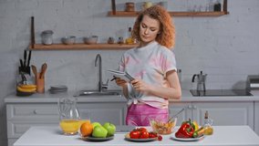 Woman with notebook weighing vegetables near salad and orange juice on table