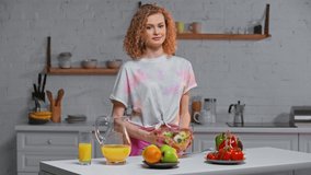 Smiling girl holding bowl with salad in kitchen